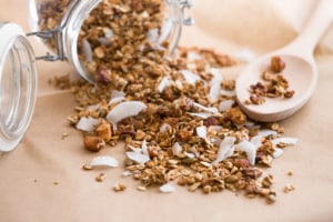 Glass jar of homemade organic granola with coconut and pecans on the baking paper background. Delicious breakfast cereal. Healthy muesli.